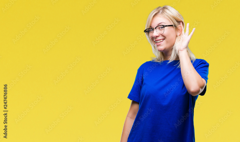 Young beautiful blonde woman wearing glasses over isolated background smiling with hand over ear listening an hearing to rumor or gossip. Deafness concept.