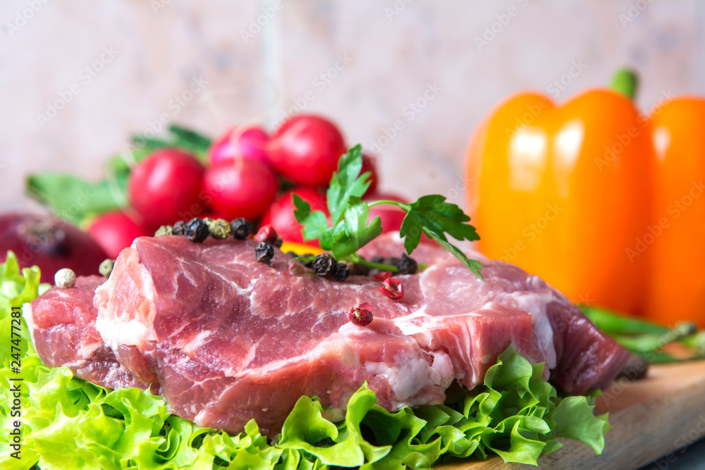 Pork-neck meat steaks on lettuce on background of radishes, tomato, red chili peppers, yellow chili peppers, green paprika, yellow paprika, red paprika, black pepper. Horizontal. Red onions, shallots Pork-neck meat steaks on lettuce on background of radishes, tomato, red chili peppers, yellow chili peppers, green paprika, yellow paprika, red paprika, black pepper. Horizontal. Red onions, shallots