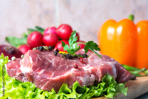Pork-neck meat steaks on lettuce on background of radishes, tomato, red chili peppers, yellow chili peppers, green paprika, yellow paprika, red paprika, black pepper. Horizontal. Red onions, shallots