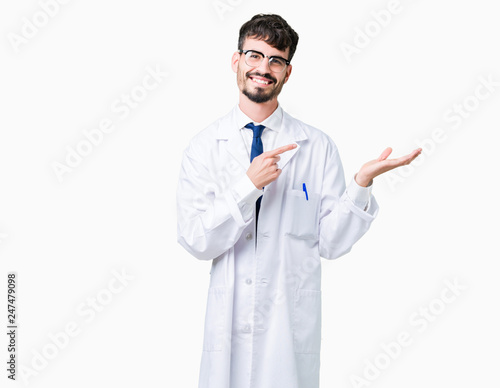 Young professional scientist man wearing white coat over isolated background amazed and smiling to the camera while presenting with hand and pointing with finger.