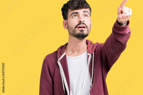 Young handsome man over isolated background Pointing with finger surprised ahead, open mouth amazed expression, something in front