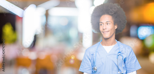 Young african american doctor man with afro hair looking away to side with smile on face, natural expression. Laughing confident.