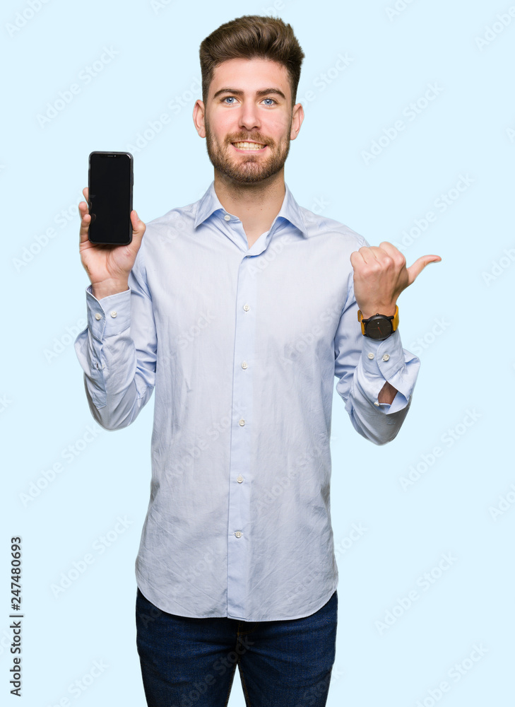 Young handsome man business showing smartphone screen pointing and showing with thumb up to the side with happy face smiling Young handsome man business showing smartphone screen pointing and showing with thumb up to the side with happy face smiling