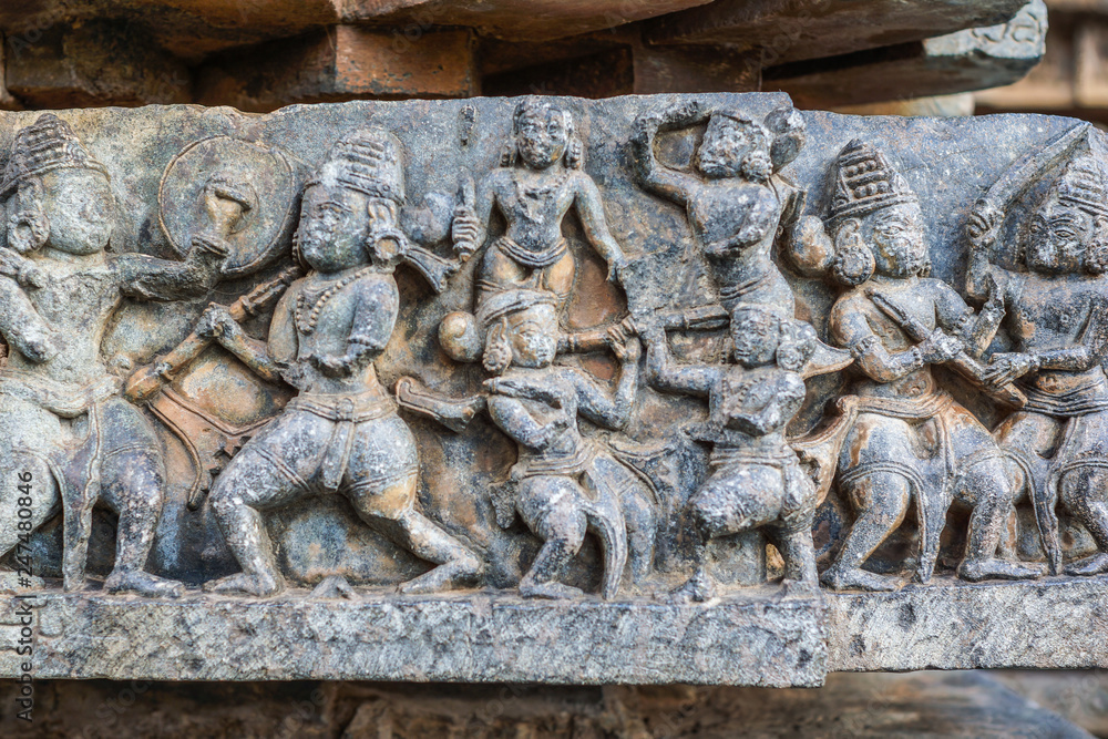 Halebidu, Karnataka, India - November 2, 2013: Hoysaleswara Temple of Shiva. Closeup of battle scene sculpture as a ribbon along wall of sanctuary. Gray brownish stone of fighting people.
