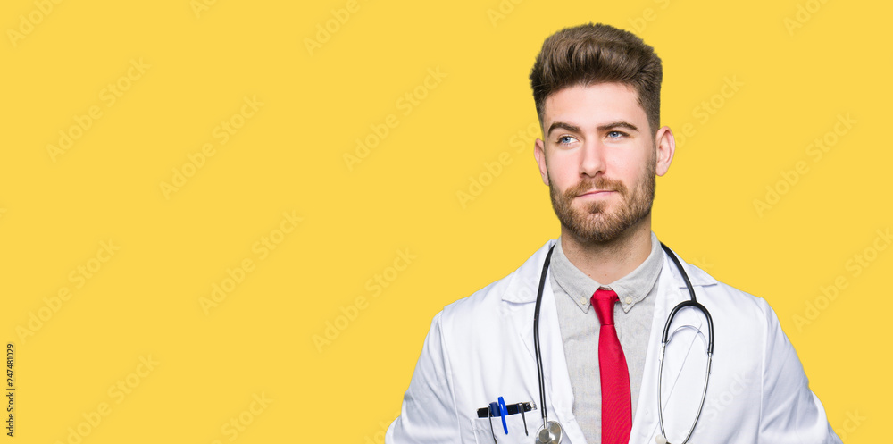 Young handsome doctor man wearing medical coat smiling looking side and staring away thinking. Young handsome doctor man wearing medical coat smiling looking side and staring away thinking.