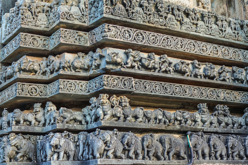 Halebidu, Karnataka, India - November 2, 2013: Hoysaleswara Temple of Shiva. Stack of ribbons of same theme statues on the side of temple building. Gray stone.