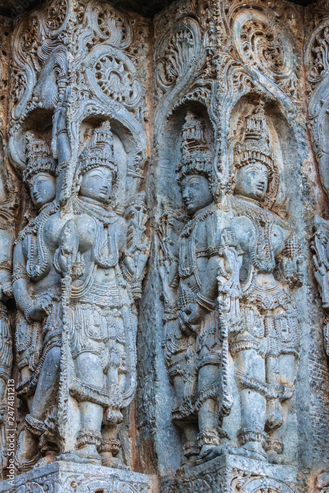 Halebidu, Karnataka, India - November 2, 2013: Hoysaleswara Temple of Shiva. Closeup of corner statues on side of the temple structure in bluish stone and some brown background.