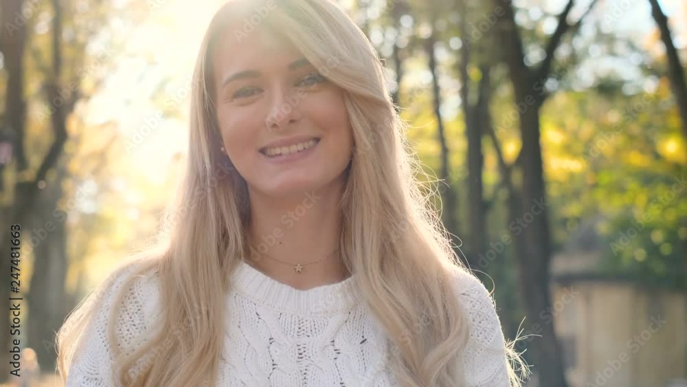 Close up portrait of woman standing sunlight in autumn park. Slow motion. Wonderful smiling girl with a lovely look and natural make up looking at camera Close up portrait of woman standing sunlight in autumn park. Slow motion. Wonderful smiling girl with a lovely look and natural make up looking at camera