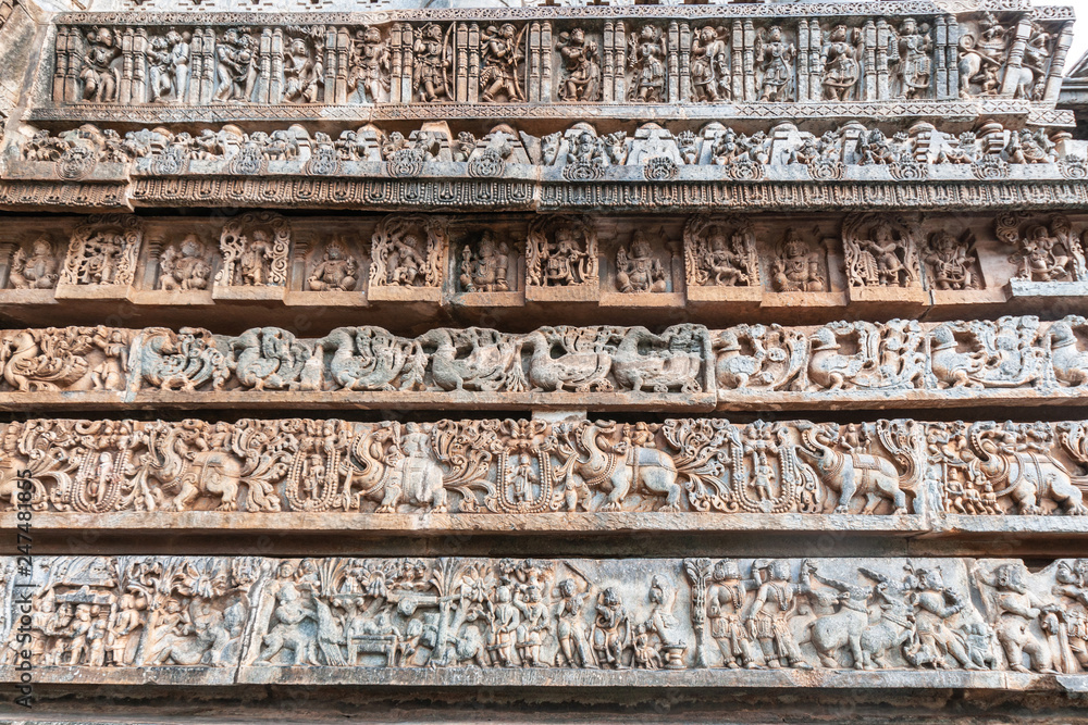 Halebidu, Karnataka, India - November 2, 2013: Hoysaleswara Temple of Shiva. Stack of ribbons of same theme statues on the side of temple building. Gray and brown stone.