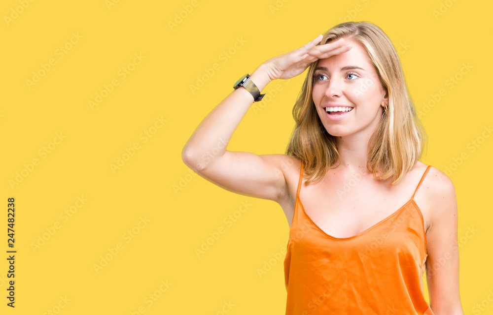 Beautiful young woman wearing orange shirt over isolated background very happy and smiling looking far away with hand over head. Searching concept. Beautiful young woman wearing orange shirt over isolated background very happy and smiling looking far away with hand over head. Searching concept.