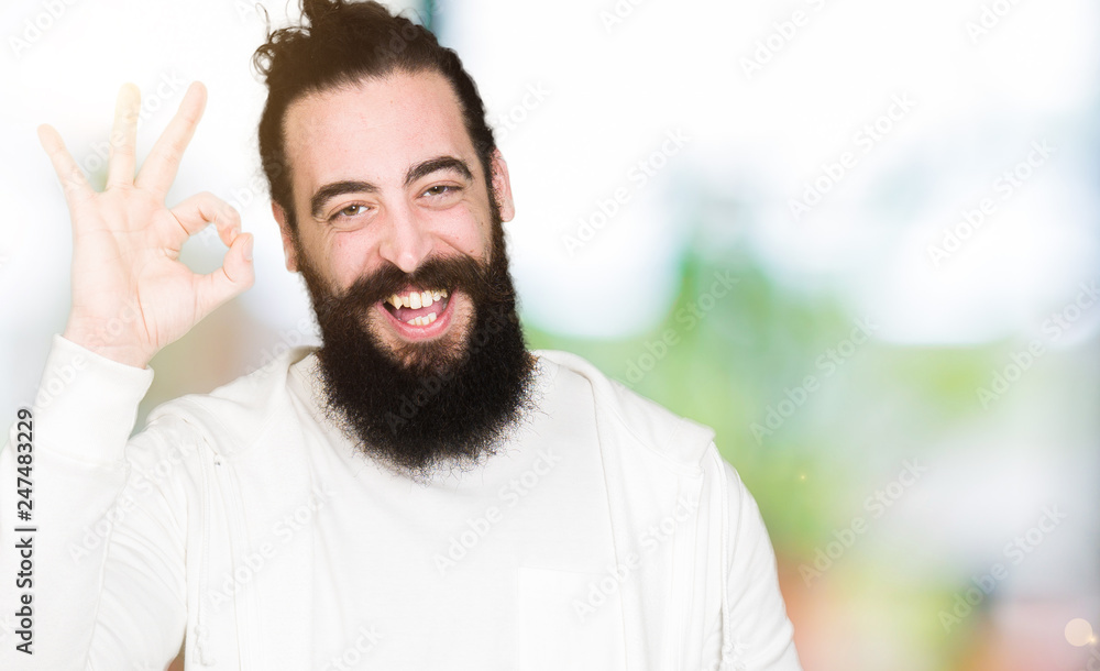 Young man with long hair and beard wearing sporty sweatshirt smiling positive doing ok sign with hand and fingers. Successful expression. Young man with long hair and beard wearing sporty sweatshirt smiling positive doing ok sign with hand and fingers. Successful expression.