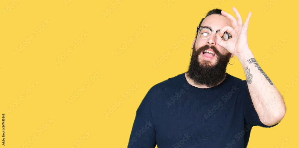 Young hipster man with long hair and beard wearing glasses doing ok gesture with hand smiling, eye looking through fingers with happy face. Young hipster man with long hair and beard wearing glasses doing ok gesture with hand smiling, eye looking through fingers with happy face.