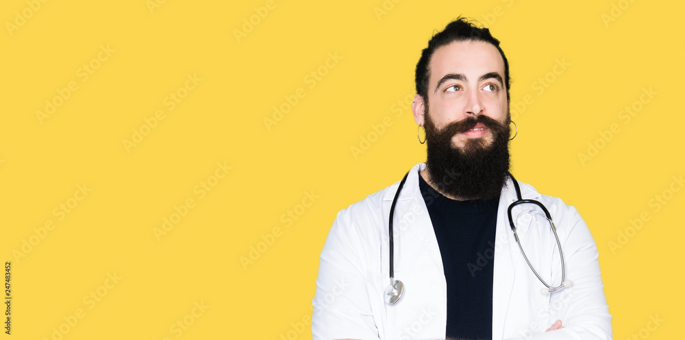 Doctor with long hair wearing medical coat and stethoscope smiling looking side and staring away thinking. Doctor with long hair wearing medical coat and stethoscope smiling looking side and staring away thinking.