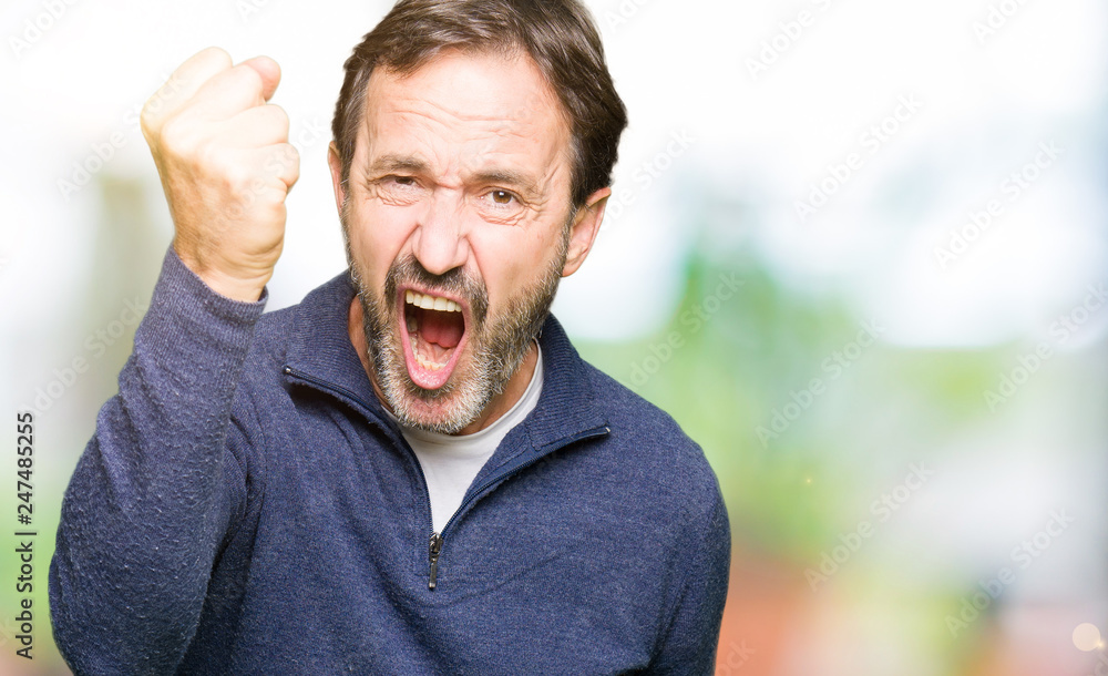 Middle age handsome man wearing a sweater angry and mad raising fist frustrated and furious while shouting with anger. Rage and aggressive concept. Middle age handsome man wearing a sweater angry and mad raising fist frustrated and furious while shouting with anger. Rage and aggressive concept.