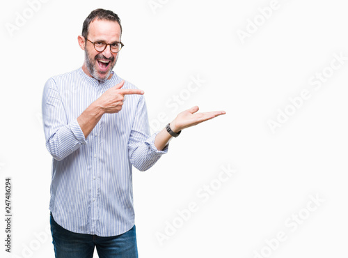 Middle age hoary senior man wearing glasses over isolated background amazed and smiling to the camera while presenting with hand and pointing with finger.