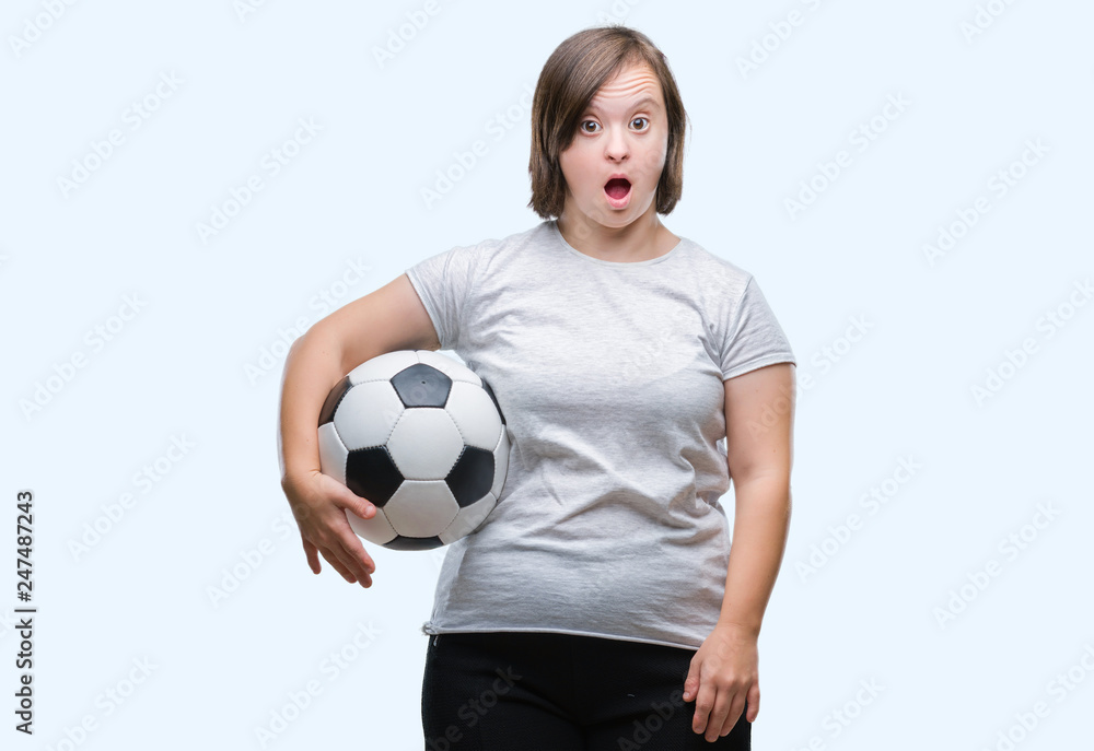 Young adult woman with down syndrome holding soccer football ball over isolated background scared in shock with a surprise face, afraid and excited with fear expression
