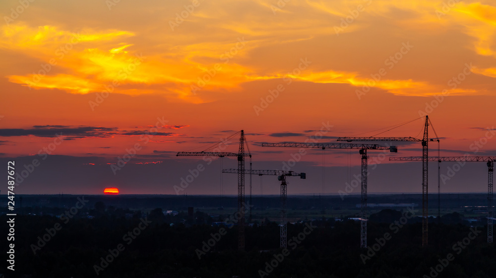 Several construction cranes on the background of colorful sunset sky