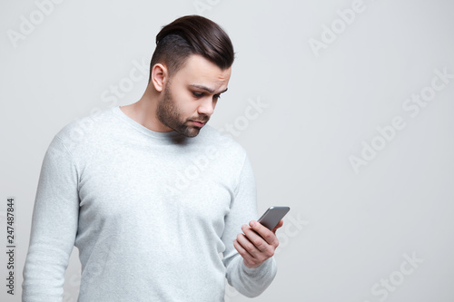 Portrait of young man looking in smartphone over white background. © Lalandrew