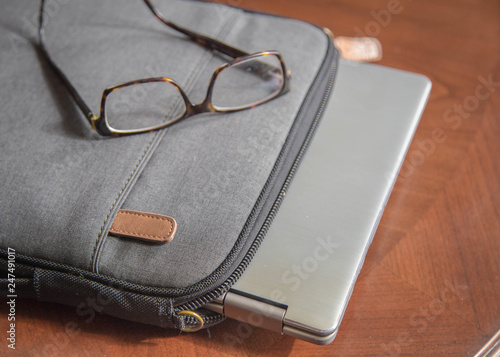 laptop sitting on wooden table with case and glasses. good for a writer, editor, author or entrepreneur. 