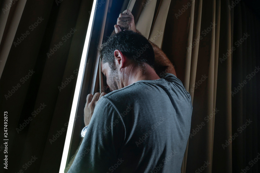 Fototapeta dramatic light portrait of young sad and depressed attractive man at home looking through room window thoughtful and pensive lost in pain broken heart suffering depression