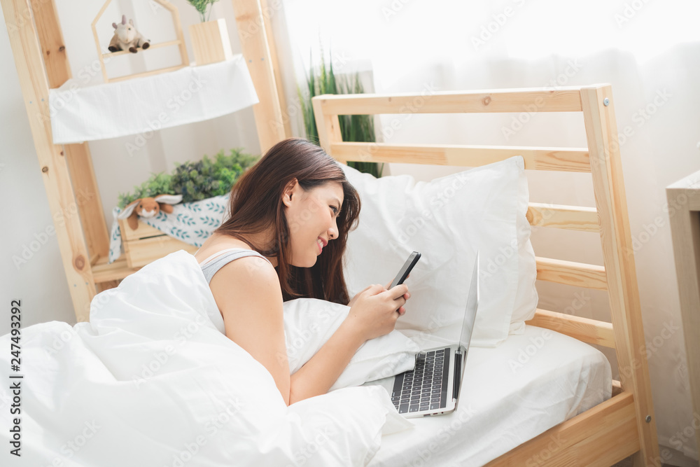 Beautiful Asian woman using laptop and smart phone in bed room for online shopping, Asian woman lifestyle concept Beautiful Asian woman using laptop and smart phone in bed room for online shopping, Asian woman lifestyle concept
