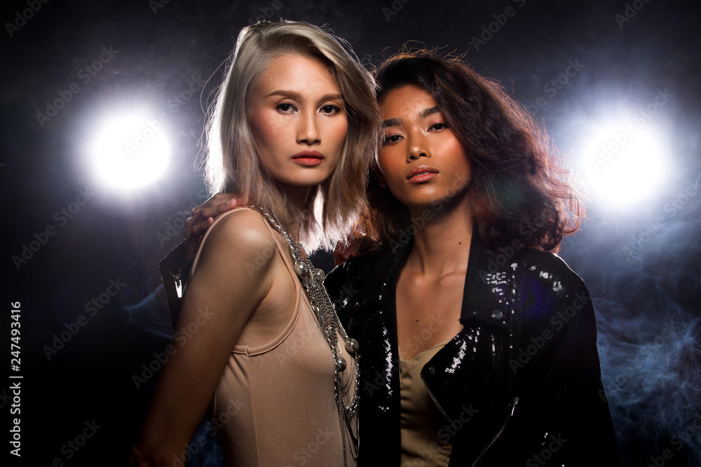 Two Fashion Young thin Asian Woman Tan skin eyes beautiful make up fashion dress lesbian look posing attractive glam look. Studio Lighting Dark Background smoke fog back rim light low exposure Two Fashion Young thin Asian Woman Tan skin eyes beautiful make up fashion dress lesbian look posing attractive glam look. Studio Lighting Dark Background smoke fog back rim light low exposure