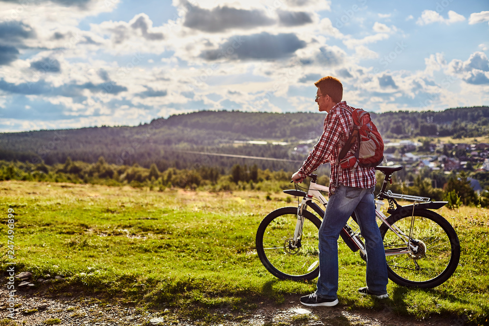 Fototapeta premium A man in nature with a bicycle on the background of mountains and blue sky