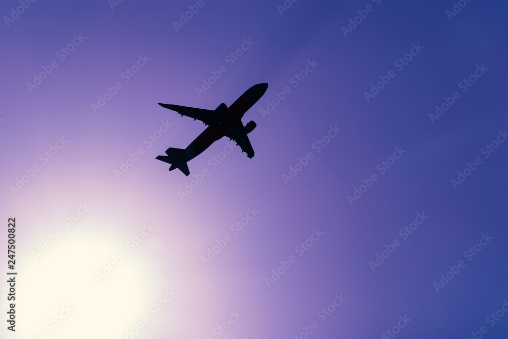 silhouette of airplane flying through the sun with purple sky background