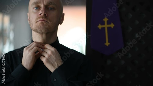 Young catholic priest dresses and buttons black shirt and a clerical colla