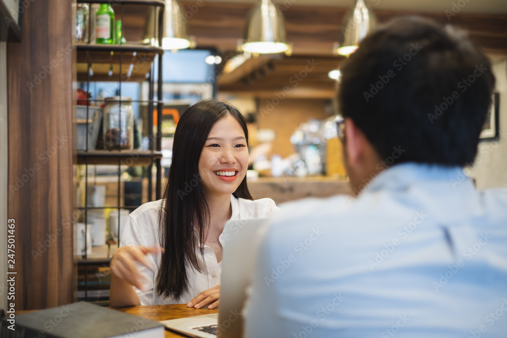 Young beautiful asian business woman in cafe, discussing business during interview with young business man Young beautiful asian business woman in cafe, discussing business during interview with young business man