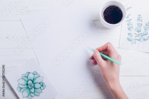  Flat lay with women hand writing on blank paper with coffee cup and green painted cards on a white wooden background. Instagram and business concept. Copy space
