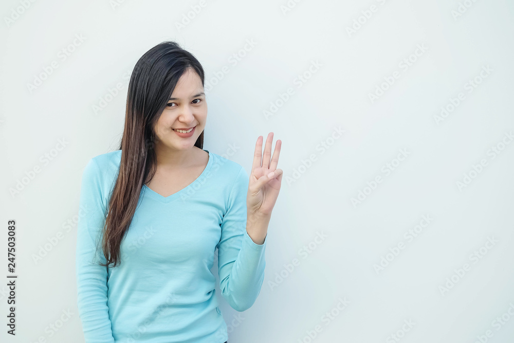 Closeup asian woman holds up three finger motion with smile face on white cement wall background with copy space Closeup asian woman holds up three finger motion with smile face on white cement wall background with copy space