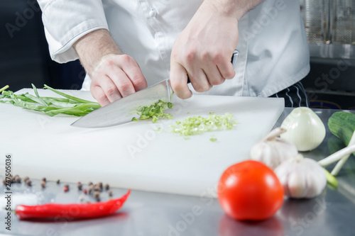 Closeup chef's hands cooking green onion for preparing healthy vegetable salad on acutting board in restaurant kitchen. Concept new lean menu, low calories speciality