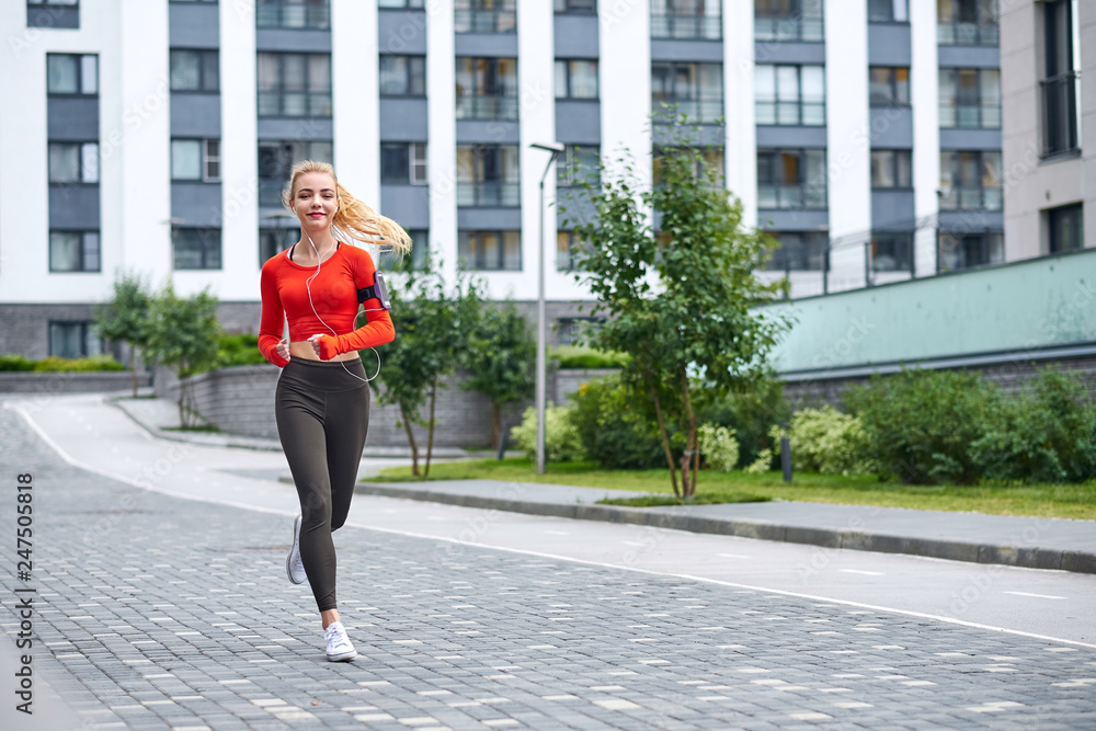 Young female runner in hoody is jogging in the city street