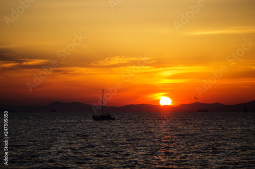 Beautiful bright sunset on the sea. A lone boat and yacht drift in the background of the sunset. © alexhitrov