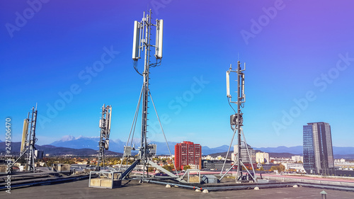 Cellular network antenna radiating and broadcasting strong power signal waves over the city on a building roof with telecommunication mast