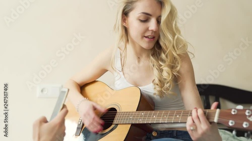 An attractive girl sings a song and plays a melody using her acoustic guitar. Her boyfriend makes a video of her singing and playing. photo