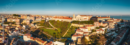 Aerial drone view of old city roofs  sunny evening in Portuguese capital, golden sunlights and dusk shadows on the ancient houses  beautiful cityscape with historical touristic routes and sunset sky © Maria Shaytor