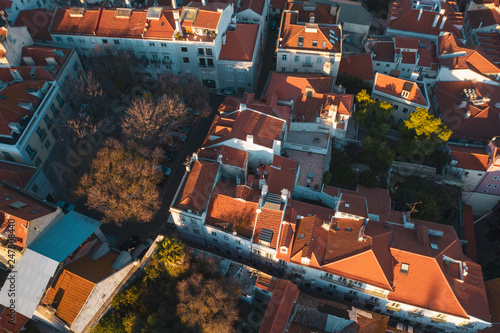 Aerial drone view of old city roofs; sunny evening in Portuguese capital, golden sunlights and dusk shadows on the ancient houses; beautiful cityscape with historical touristic routes and sunset sky