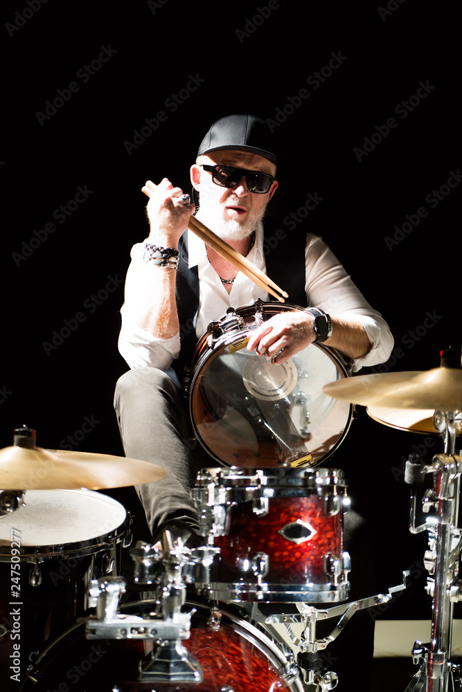 Fototapeta premium Drummer with a drumsticks in his hands sits behind drum kit on the black background