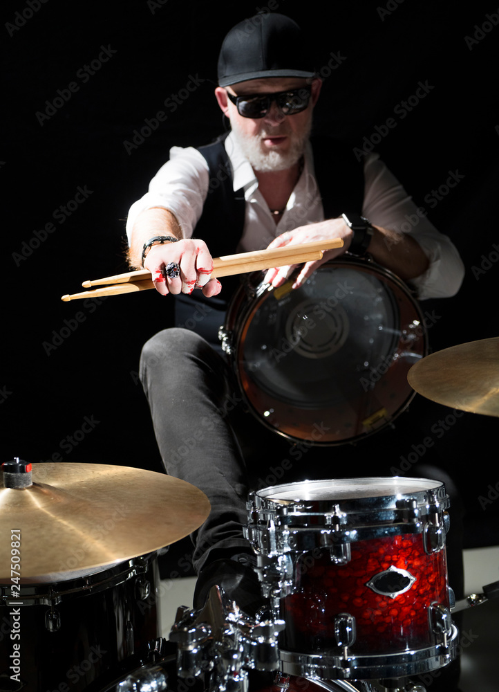 Drummer with a drumsticks in his hands sits behind drum kit on the black background Drummer with a drumsticks in his hands sits behind drum kit on the black background