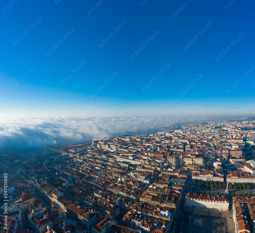Aerial; panoramic drone view of foggy Lisbon morning; impending clouds over the ancient ginger roofs; blue skyline and bright sun in portuguese historical capital; touristic areas, old narrow streets