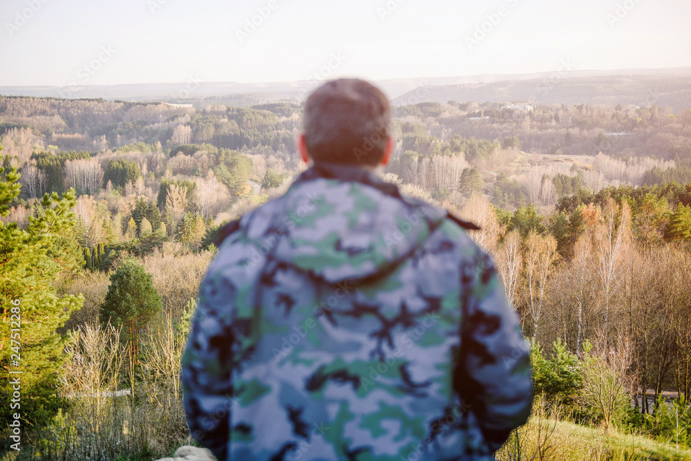 healthy man in jacket watching at beautiful spring mountain forest landscape during recreational hiking