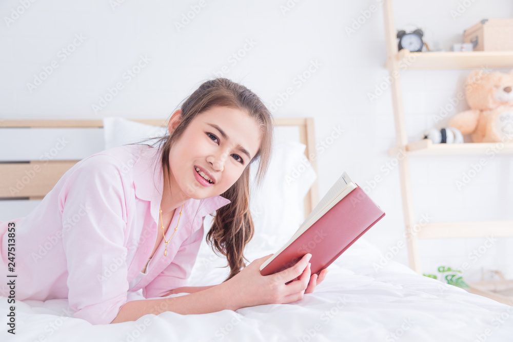 Beautiful asian girl lying on bed and reading book in the morning Beautiful asian girl lying on bed and reading book in the morning