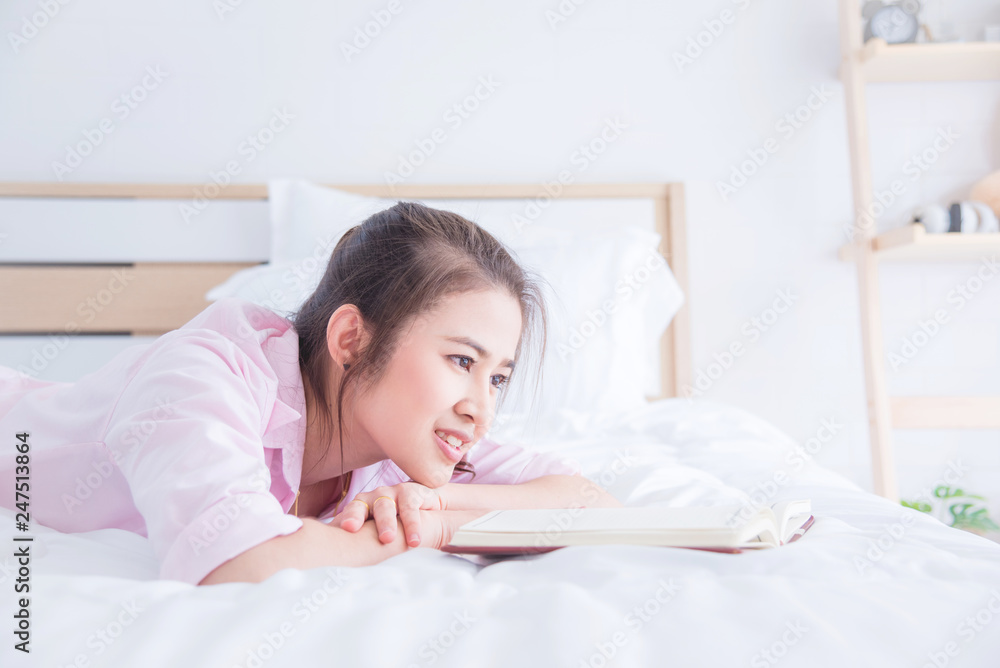 Beautiful asian girl lying on bed and reading book in the morning Beautiful asian girl lying on bed and reading book in the morning