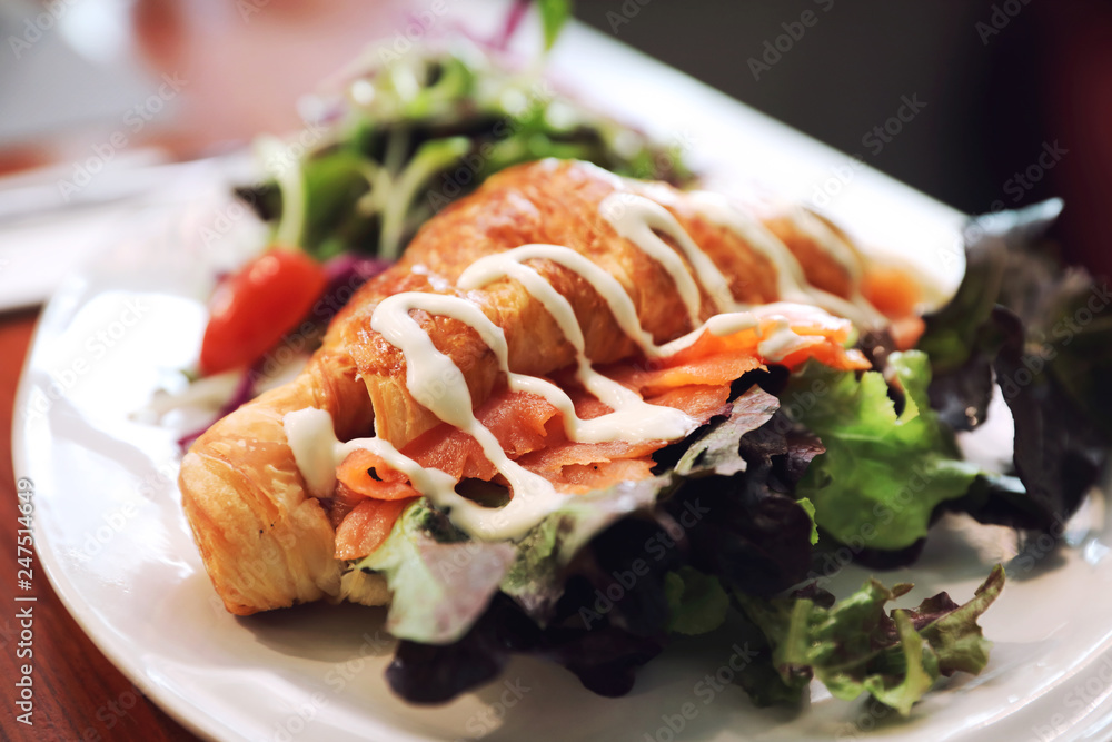 Croissant bread with salmon and salad on wooden background