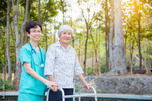 Disabled senior asian woman walking with assistance from nurse in hospital park