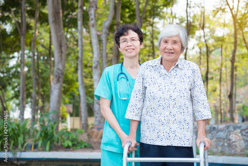 Disabled senior asian woman walking with assistance from nurse in hospital park