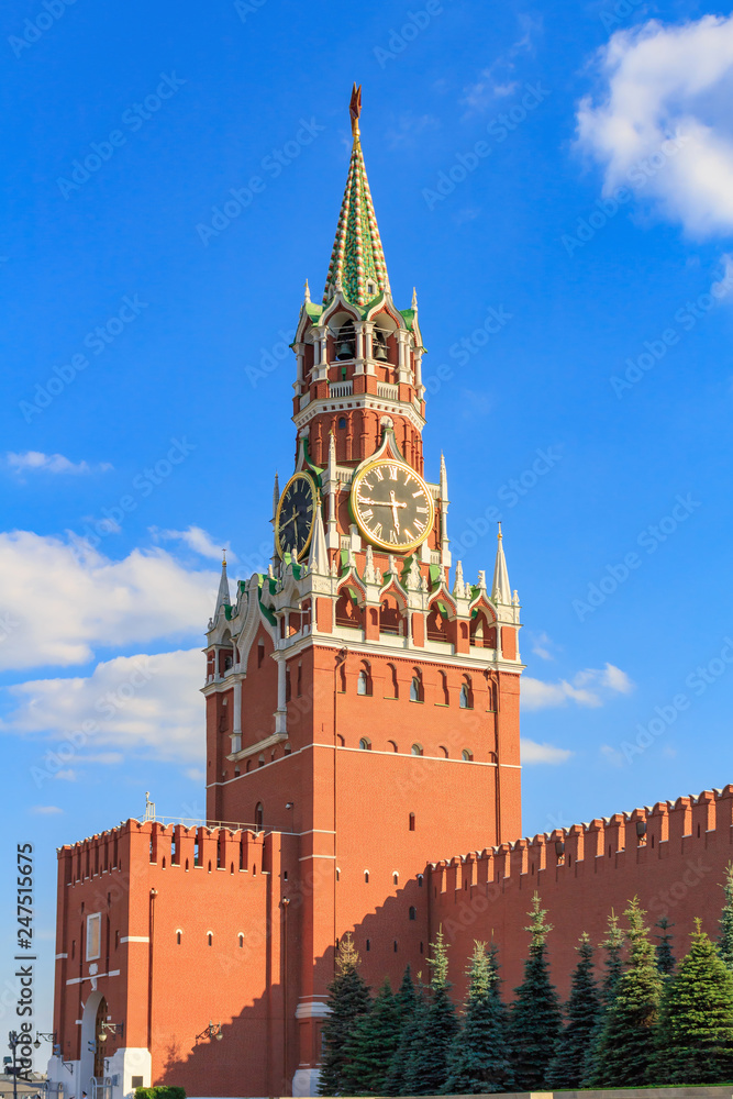Spasskaya tower and Kremlin wall on a background of green spruces at sunny day against blue sky Spasskaya tower and Kremlin wall on a background of green spruces at sunny day against blue sky