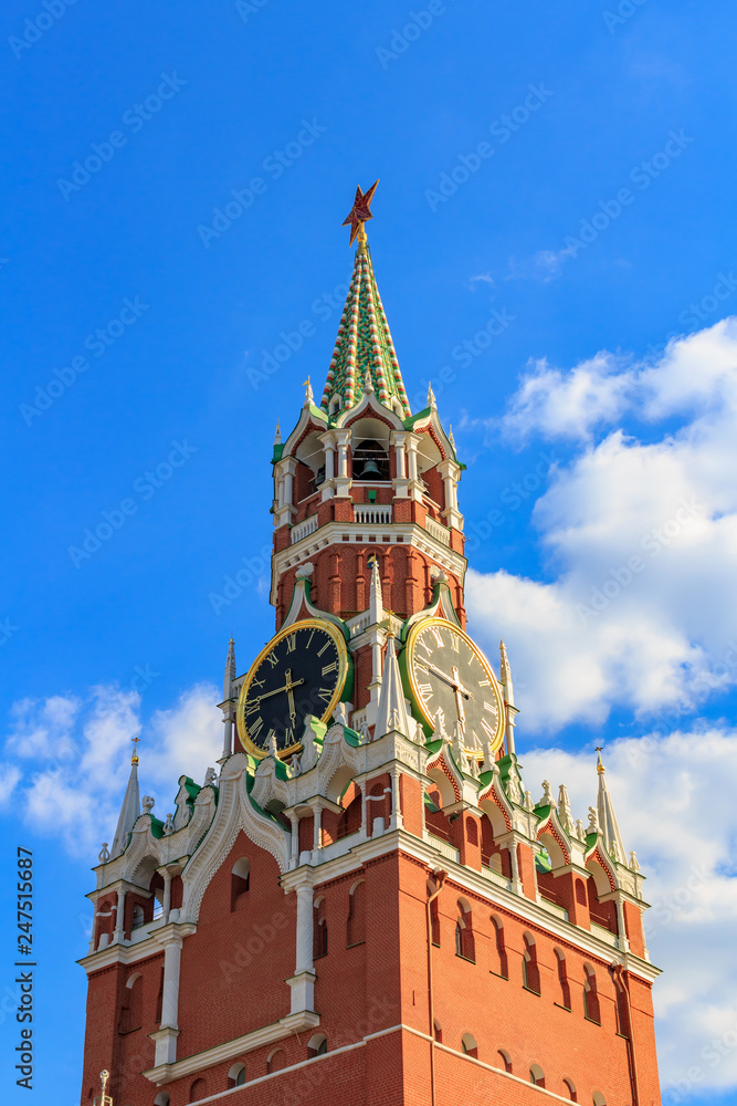 Spasskaya tower of Moscow Kremlin with ruby red star and chimes clock on a background of blue sky with white clouds at sunny day